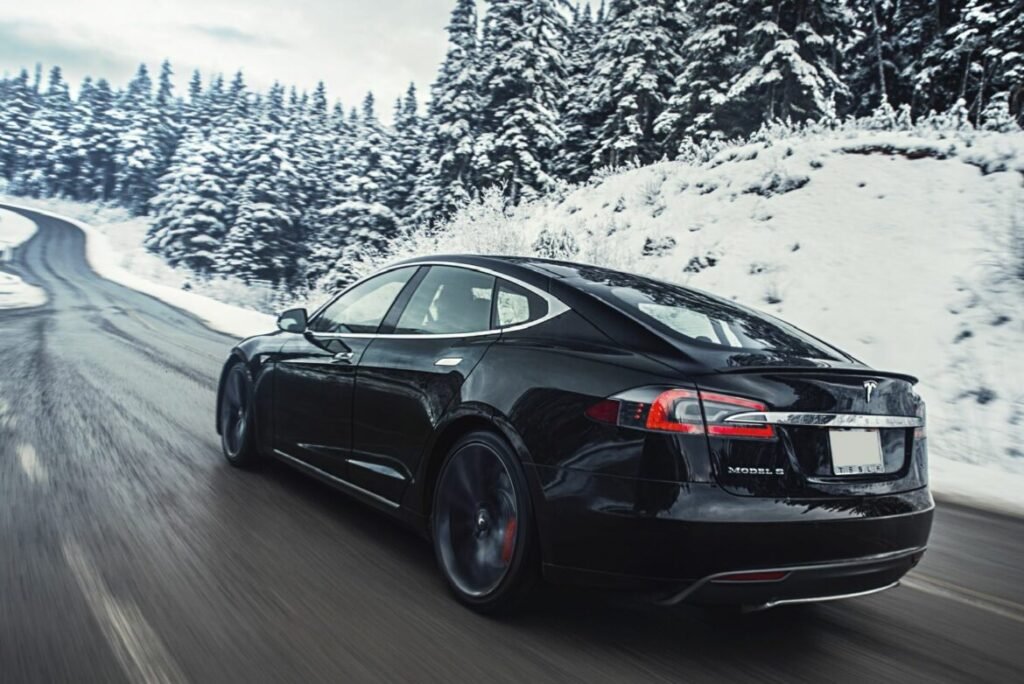 Une Tesla roule sur une route en forêt en plein hiver